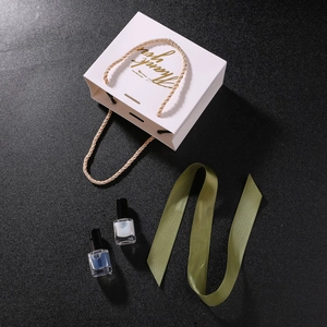 Macro shot of white Thank You gift bag with gold braided handles and elegant foil lettering