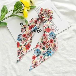 Close-up of floral chiffon scrunchie with long ribbons on white textured fabric