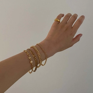 Close-up of stacked gold Figaro and curb chain bracelets with a minimalist ring on a hand