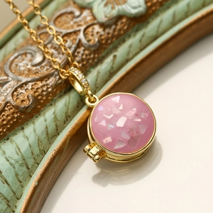 Close-up of a gold-plated round locket pendant with pink stones on a vintage frame