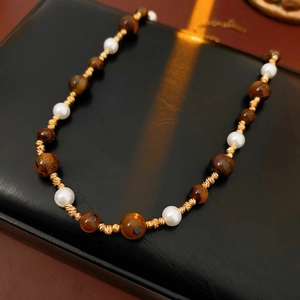 Detail of tiger eye stone and pearl necklace on black leather with professional lighting