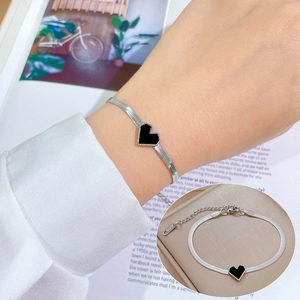 Silver stainless steel snake chain bracelet with black heart charm on female wrist