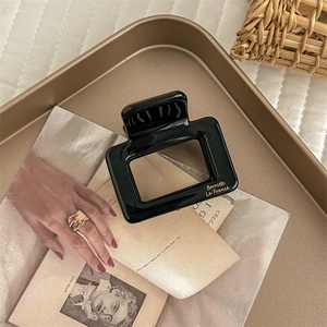 Detail of square black acetate hair claw with gold lettering on a vintage tray