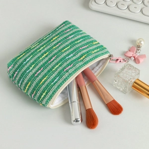 Macro shot of green tweed cosmetic pouch with pearl bow charm and makeup brushes