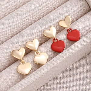Macro shot of gold and red heart drop earrings arranged in a beige fabric jewelry box