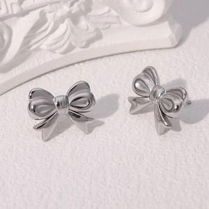 Detail shot of silver bow stud earrings with polished metallic luster on textured background