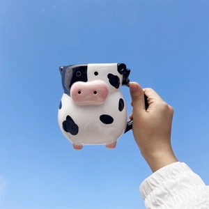 Detail of cow-shaped ceramic coffee mug held against a clear blue sky background