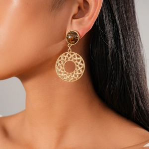 Close-up of golden hollow mesh earrings with tiger eye stone on model's earlobe