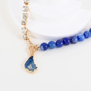 Detail von blauen Marmorperlen und unregelmäßigem Edelsteinanhänger an goldener Kette