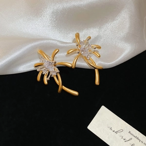 Close-up of golden flower stud earrings with white cubic zirconia on silk background