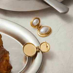 Macro view of vintage gold-plated earrings with oval white pearls on a steel tray