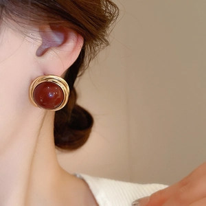 Close-up of red round pearl earrings with vintage gold metal spiral frame on model