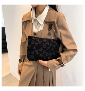 Detail of black fabric clutch featuring 3D floral textures held by a model in a trench coat