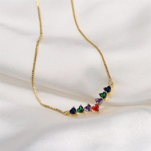 Gold fan pendant necklace with colorful heart-shaped zircons on white silk background