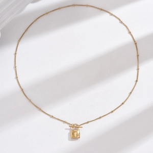 Elegant gold bead chain necklace with white shell lock pendant on white background