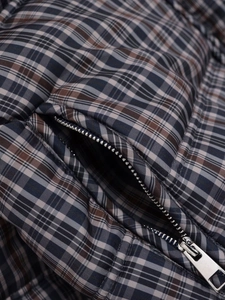 Macro shot of silver metal zipper pocket on navy blue and brown plaid padded jacket