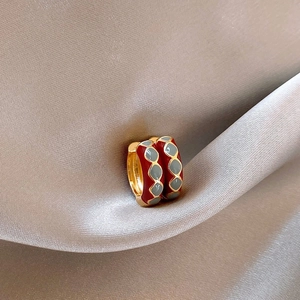 Detail of red enamel earrings with blue diamond patterns on champagne satin fabric