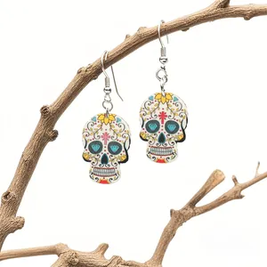 Colorful sugar skull acrylic drop earrings displayed on a rustic wooden branch