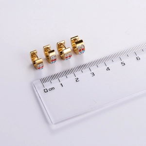 Golden stainless steel hinged earrings with colorful zircon stones shown with a ruler
