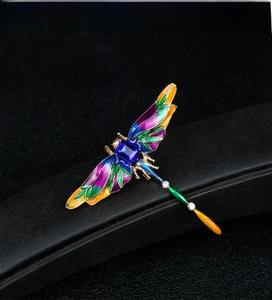 Macro detail of enamel dragonfly brooch with blue gemstone and gold-tone metal frame
