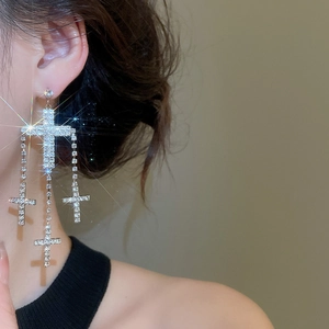 Close-up of sparkling silver cross tassel earrings with rhinestones on a model's ear