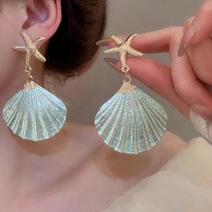 Close-up of light blue shell earrings with gold starfish stud worn by a model