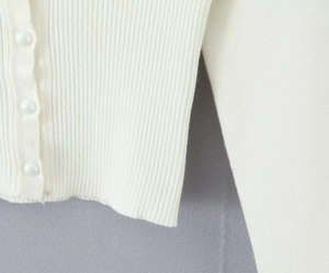 Dettaglio del cardigan bianco con trama a coste e bottoni di perle eleganti