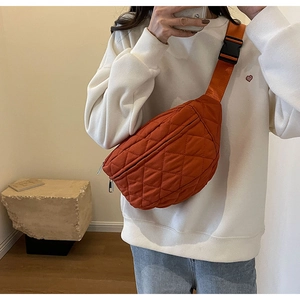 Detail of orange quilted crossbody bag featuring adjustable strap and black buckle closure