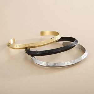 Detail of titanium steel C-shaped bracelets with embossed geometric patterns in gold, black, and silver