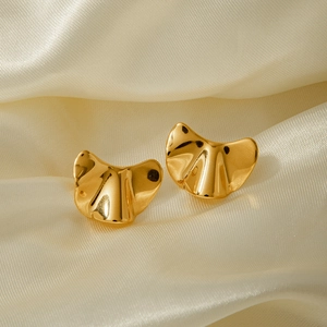 Close-up of golden 18k stainless steel earrings with fan-shaped textured design on silk