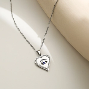 Silver heart necklace with blue evil eye pendant and crystal pave on white surface