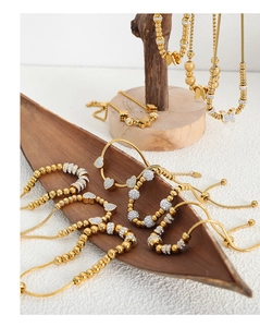 Detail of gold beaded bracelets with zircon butterfly and heart charms on a wooden tray
