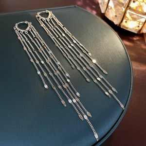 Close-up of silver sequin chain tassel earrings on a premium green display stand