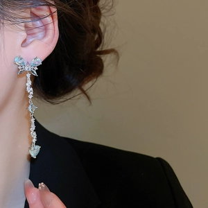 Close-up of dangling silver tassel earrings with blue butterfly and heart-shaped crystals