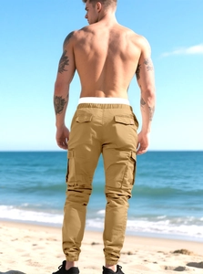 Detail of khaki cargo joggers showing cotton twill fabric and back flap pockets by the sea
