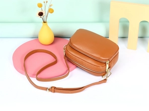 Detailopname van de bruine lederen crossbodytas met lychee-patroon en metalen ritsen