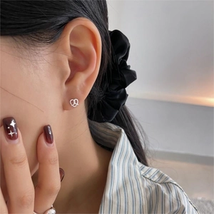 Detail view of model wearing small twisted silver heart stud earring in 925 sterling silver