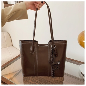 Detail of dark brown tote bag with white contrast stitching and cat pendant