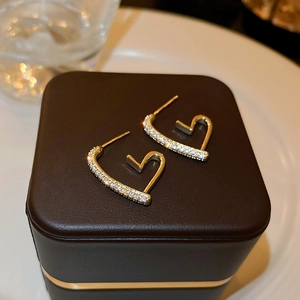 Close-up of gold-plated heart earrings with cubic zirconia on a leather jewelry box