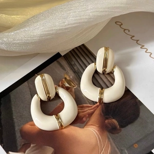 Detailed shot of retro C-shaped French enamel earrings in white and gold on soft fabric