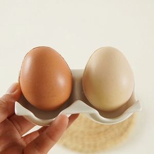 Double-slot white ceramic egg holder tray with a smooth glazed finish and wavy edges