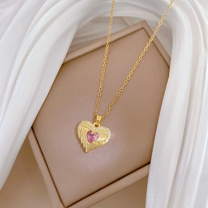 Detail of gold heart pendant with pink gemstone and angel wings on a silk background