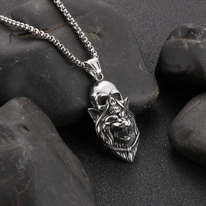 Close-up of silver skull and lion pendant on box chain over wet black pebbles