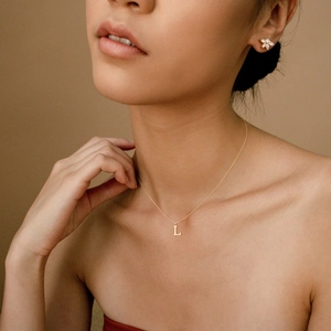 Close-up of minimalist gold initial L necklace and sparkling flower stud earrings on model