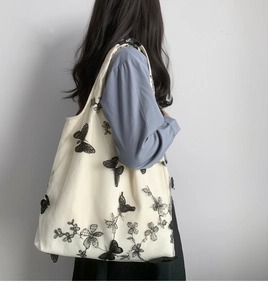 Detail shot of white canvas tote bag with black butterfly embroidery on female model