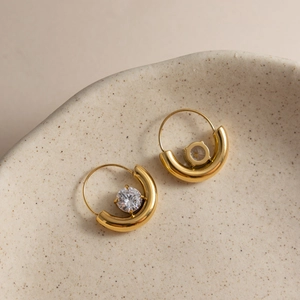 Close-up of 18K gold hoop earrings with round white zircon in a ceramic jewelry tray