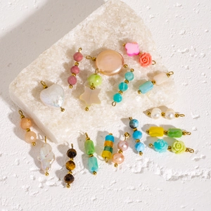 Colorful natural stone and baroque pearl jewelry charms with gold rings on white stone