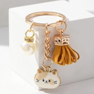 Close-up of golden keychain with tassel, pearl charm, and cute cat pendant details