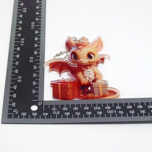 Detail showing an orange acrylic dragon charm on a gift box with a metal bead chain