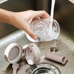 Clear glass seasoning container with pink plastic lid being washed in a steel sink
